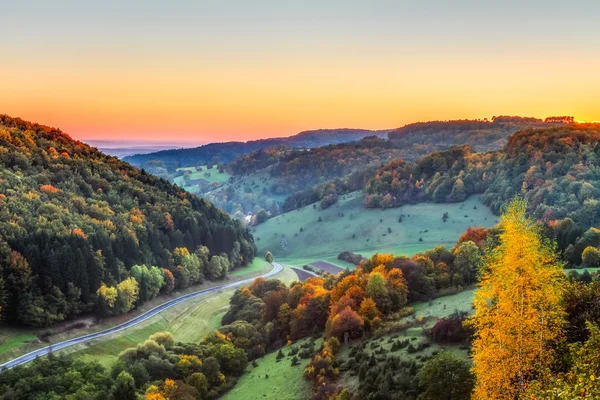 Idyllische Herbstkulisse mit farbenfrohen orange-goldenen Bäumen an einer schönen Landstraße in den felsigen Jurabergen Bayerns. Sonnenuntergang im Herbst mit herrlich klarem Himmel in der ländlichen Landschaft. — Stockfoto