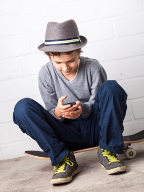 cool çocuk onun kaykay üzerinde oturan bir smartphone holding