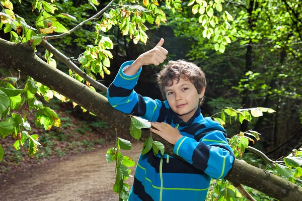 Tiener leunend op een stam, thumbs-up. — Stockfoto