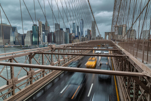 New York, USA - OCTOBER 11, 2018: View of the Manhattan skyline on a very cloudy day with moving cars, one yellow taxi on the Brooklyn Bridge in the foreground.