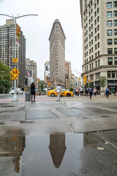 美国纽约 2018年10月11日 前面有一辆黄色出租车和一个有倒影的水坑的扁铁建筑 图库图片