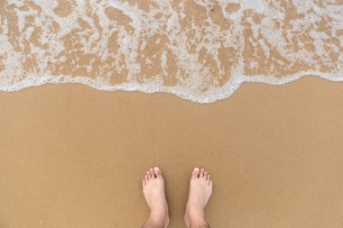 Pürüzsüz sahilde ayakkabısız bir adamın ayakları ve yukarıdan çekilen fotoğraflarla denizin yumuşak köpüğü. Deniz ve plaj fotoğraflarını kopyala