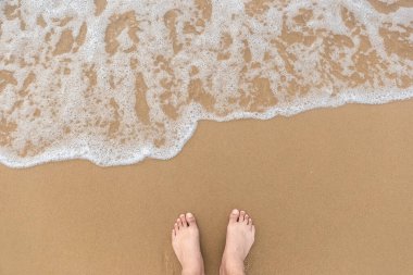 Pürüzsüz sahilde ayakkabısız bir adamın ayakları ve yukarıdan çekilen fotoğraflarla denizin yumuşak köpüğü. Deniz ve plaj fotoğraflarını kopyala