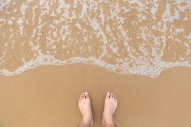 Pürüzsüz sahilde ayakkabısız bir adamın ayakları ve yukarıdan çekilen fotoğraflarla denizin yumuşak köpüğü. Deniz ve plaj fotoğraflarını kopyala