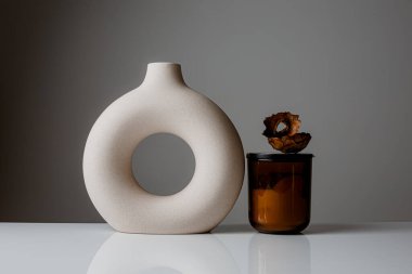 Cozy home and Spa concept. Hygge. Modern stylish and minimal round vase with dried lagurus grass, seashell candles and palm leaves in front of a grey wall.