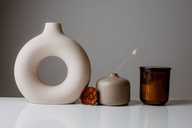 Cozy home and Spa concept. Hygge. Modern stylish and minimal round vase with dried lagurus grass, seashell candles and palm leaves in front of a grey wall.