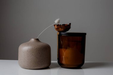 Cozy home and Spa concept. Hygge. Modern stylish and minimal round vase with dried lagurus grass, seashell candles and palm leaves in front of a grey wall.