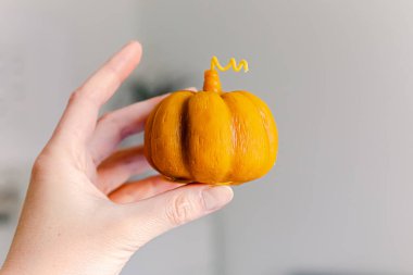 Still life, candle, rowan berry and pumpkin in the living room on a table, home decor in a cozy house. Autumn weekend concept, blanket and plaid. Small pumpkin candle in a woman hand.