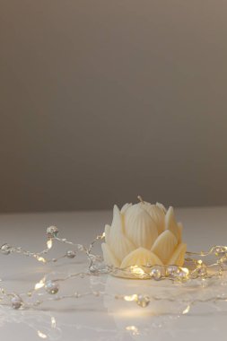 Small lotus candle in an transparent lotus shaped glass candle holder laying on glass mirrow white table. Christmas concept.