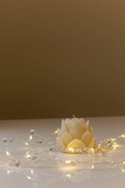 Small lotus candle in an transparent lotus shaped glass candle holder laying on glass mirrow white table. Christmas concept.
