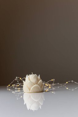 Small lotus candle in an transparent lotus shaped glass candle holder laying on glass mirrow white table. Christmas concept.