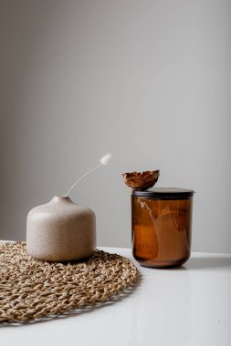 Cozy home interior decor, aromatic candles in glass glowingon white and grey background with natural oil, selective focus of fluffy bunny tail grass, brown jar, lotus flower candle, round matt ceramic