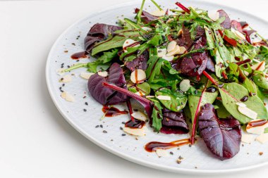 Spinach salad on white, with beetroot, arugula, balsamic vinegar, black sesame seeds, almond petals and feta cheese over light grey slate. Top view.