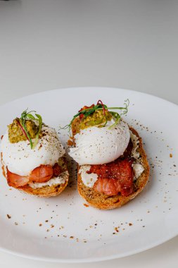 Avocado eggs benedict with pesto sauce, grilled bacon, pepper, cream cheese Philadelphia. Poached eggs on healthy bread toast with hollandaise sauce. Cut egg. The yolk flows out. Micro greens.
