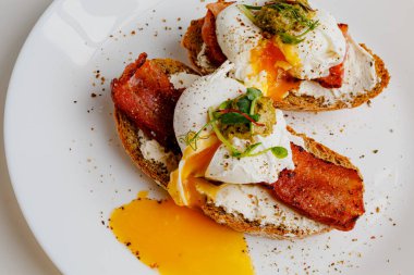 Avocado eggs benedict with pesto sauce, grilled bacon, pepper, cream cheese Philadelphia. Poached eggs on healthy bread toast with hollandaise sauce. Cut egg. The yolk flows out. Micro greens.