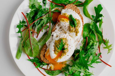 Avocado egg benedict with cream cheese Philadelphia. Poached eggs on healthy bread toast with hollandaise sauce. Cut egg. The yolk flows out. Green salad arugula leaves.