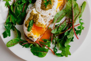 Avocado egg benedict with cream cheese Philadelphia. Poached eggs on healthy bread toast with hollandaise sauce. Cut egg. The yolk flows out. Green salad arugula leaves.