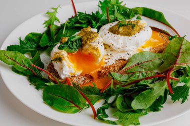 Avocado egg benedict with cream cheese Philadelphia. Poached eggs on healthy bread toast with hollandaise sauce. Cut egg. The yolk flows out. Green salad arugula leaves.