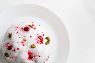 Blueberry muffin with whipped cream. Easter muffin cake with pistachios and cranberry and easter decorations on a white plate. Dragon lilac easter eggs. White background. Copy space.