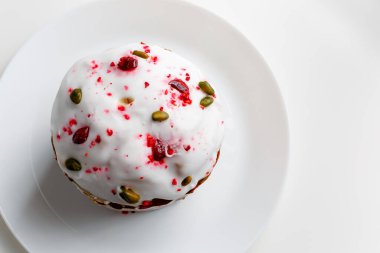 Blueberry muffin with whipped cream. Easter muffin cake with pistachios and cranberry and easter decorations on a white plate. Dragon lilac easter eggs. White background. Copy space.