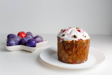Blueberry muffin with whipped cream. Easter muffin cake with pistachios and cranberry and easter decorations on a white plate. Dragon lilac easter eggs. White background. Copy space.
