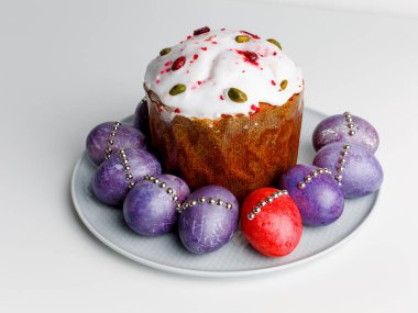 Blueberry muffin with whipped cream. Easter muffin cake with pistachios and cranberry and easter decorations on a white plate. Dragon lilac easter eggs. White background. Copy space.