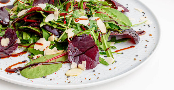 Spinach salad on white, with beetroot, arugula, balsamic vinegar, black sesame seeds, almond petals and feta cheese over light grey slate. Top view.