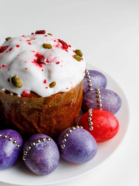 Blueberry muffin with whipped cream. Easter muffin cake with pistachios and cranberry and easter decorations on a white plate. Dragon lilac easter eggs. White background. Copy space.
