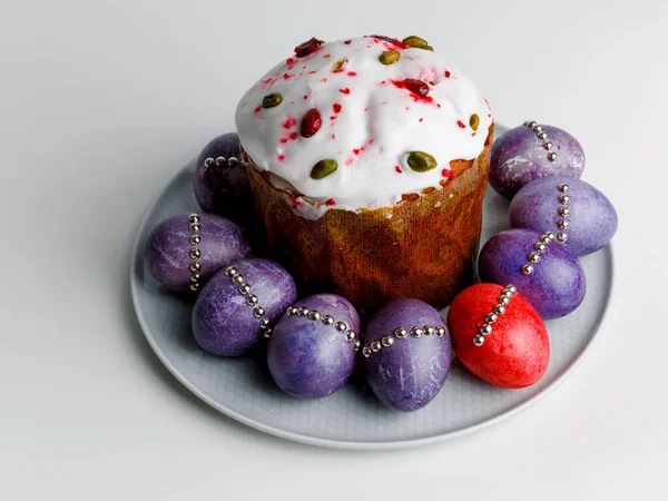 Blueberry muffin with whipped cream. Easter muffin cake with pistachios and cranberry and easter decorations on a white plate. Dragon lilac easter eggs. White background. Copy space.