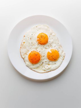 Three fried eggs with pepper and salt on a white plate. White background.