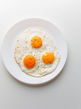 Three fried eggs with pepper and salt on a white plate. White background.