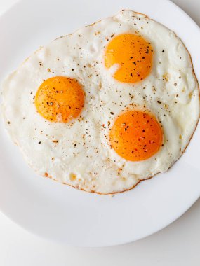 Three fried eggs with pepper and salt on a white plate. White background.