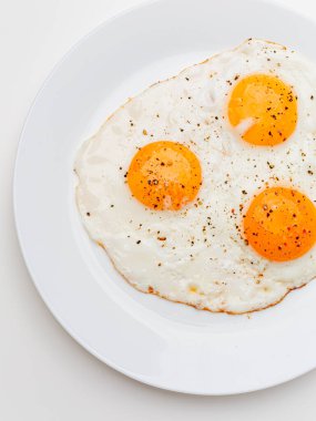 Three fried eggs with pepper and salt on a white plate. White background.