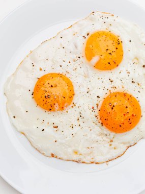 Three fried eggs with pepper and salt on a white plate. White background.