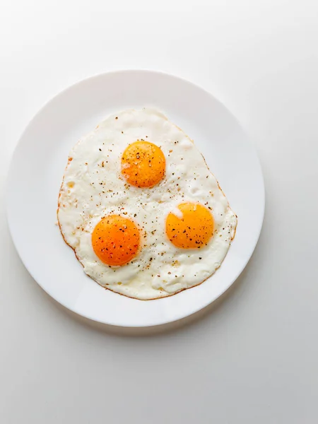 Three Fried Eggs Pepper Salt White Plate White Background — Zdjęcie stockowe