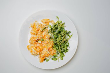 Scrambled eggs with micro greens and beans on white plate over white stone background. American breakfast, healthy morning food. Top view, flat lay.
