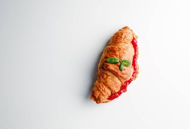 Delicious fresh croissant on a white and light grey background. Croissant with strawberry and lemongrass jam and mint leaves. French breakfast. Morning. Top view.