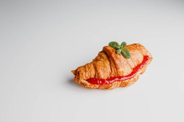 Delicious fresh croissant on a white and light grey background. Croissant with strawberry and lemongrass jam and mint leaves. French breakfast. Morning. Top view.
