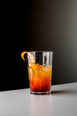 Fruit healthy cocktail from mango juice, orange peel spiral and ice on dark black background.