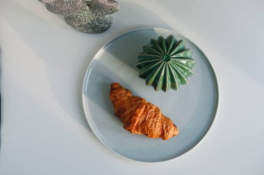 Delicious fresh croissant on a white and light grey background. Croissant with mint color glass vase, Wicker basket, metal and ceramic cactus. French breakfast. Morning. Top view.