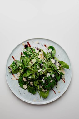 Spinach salad on white, with beetroot, arugula, balsamic vinegar, black sesame seeds, almond petals and feta cheese over light grey slate. Top view.