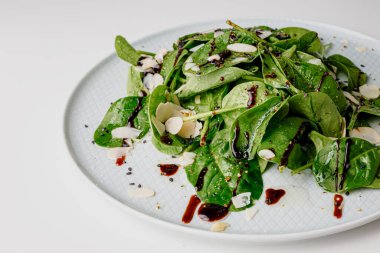 Spinach salad on white, with beetroot, arugula, balsamic vinegar, black sesame seeds, almond petals and feta cheese over light grey slate. Top view.