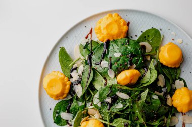 Squash and spinach salad on white, with beetroot, arugula, balsamic vinegar, black sesame seeds, almond petals and feta cheese over light grey slate. Top view.