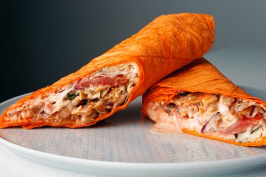 Shawarma sandwich gyro- fresh roll of thin lavash (pita bread) filled with grilled meat, mushrooms, cheese, cabbage, carrots, sauce, green. Traditional Eastern snack. On dark grey background