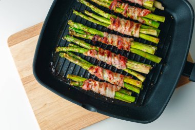 Asparagus with bacon on grilled pan. Grilled green asparagus wrapped with bacon. Asparagus baked with bacon and spices. Healthy food. Top view. Free space for text. Bacon wrapped asparagus on white.
