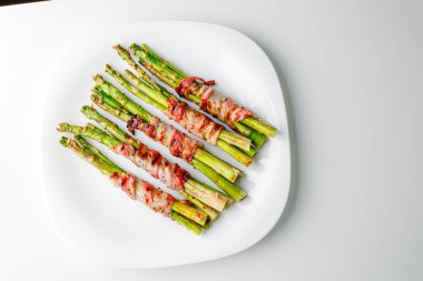 Grilled green asparagus wrapped with bacon. Asparagus baked with bacon and spices. Healthy food. Top view. Free space for your text. Bacon wrapped asparagus on white plate.