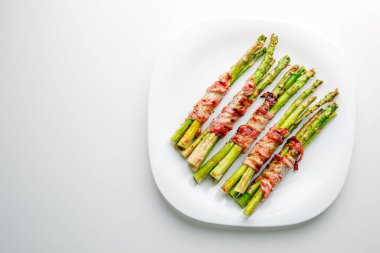 Grilled green asparagus wrapped with bacon. Asparagus baked with bacon and spices. Healthy food. Top view. Free space for your text. Bacon wrapped asparagus on white plate.