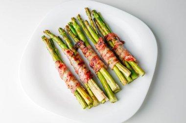 Grilled green asparagus wrapped with bacon. Asparagus baked with bacon and spices. Healthy food. Top view. Free space for your text. Bacon wrapped asparagus on white plate.