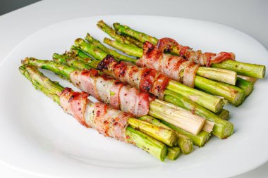 Grilled green asparagus wrapped with bacon. Asparagus baked with bacon and spices. Healthy food. Top view. Free space for your text. Bacon wrapped asparagus on white plate.