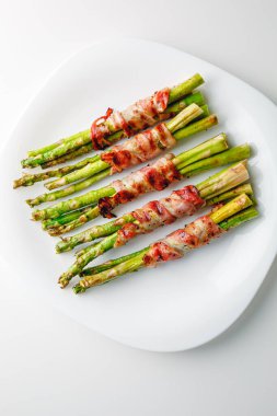 Grilled green asparagus wrapped with bacon. Asparagus baked with bacon and spices. Healthy food. Top view. Free space for your text. Bacon wrapped asparagus on white plate.